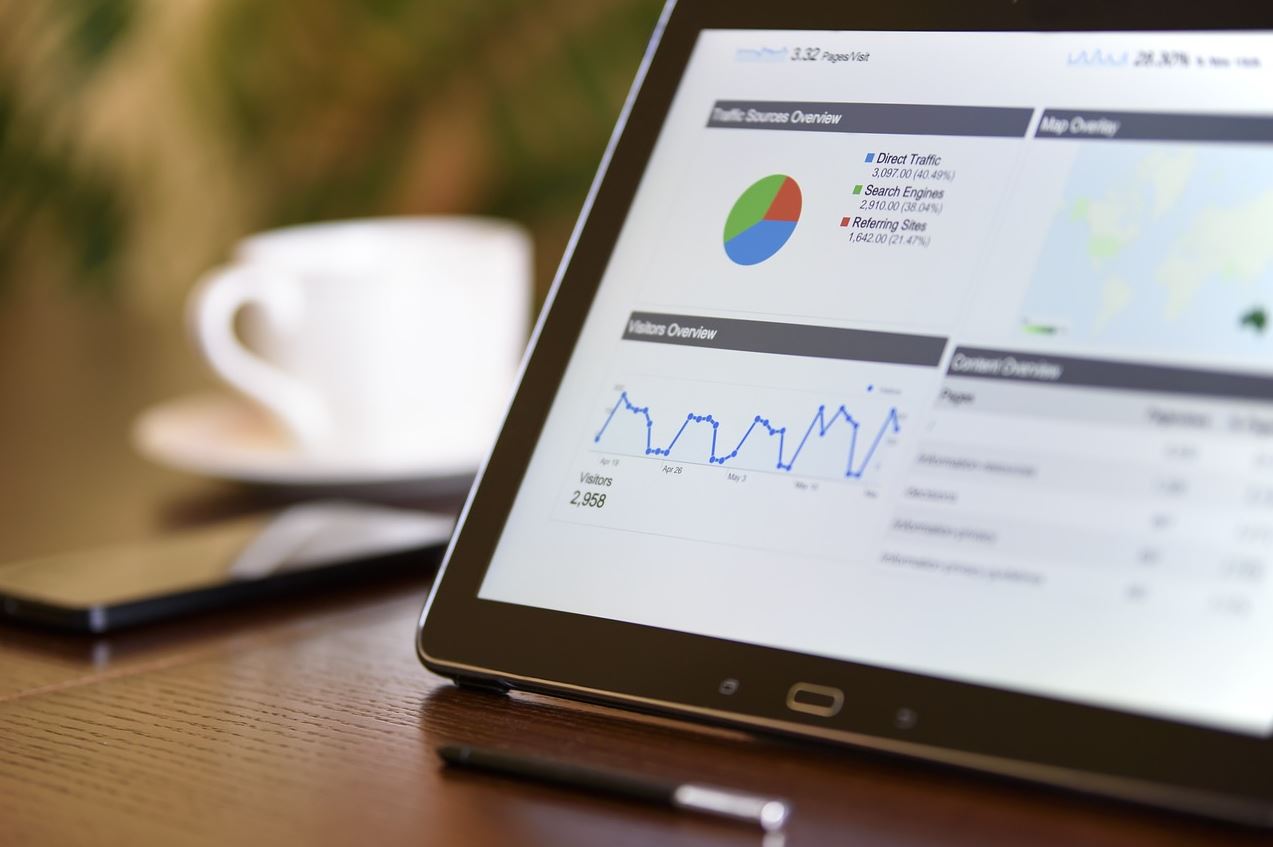 A laptop with data on the screen next to a cup, pen and mobile